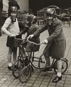 Children playing on bicycles wearing their gas masks, ca. 1940s